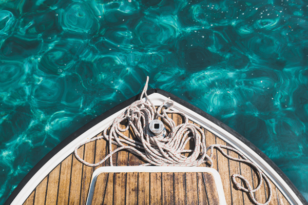 The bow of a wooden boat with line coiled on the decks is pictured here resting in still blue water.