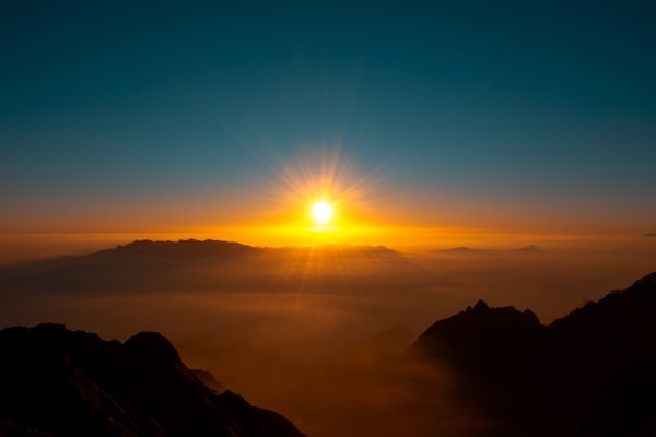 Sun rises behind clouds, viewed between two mountain peaks