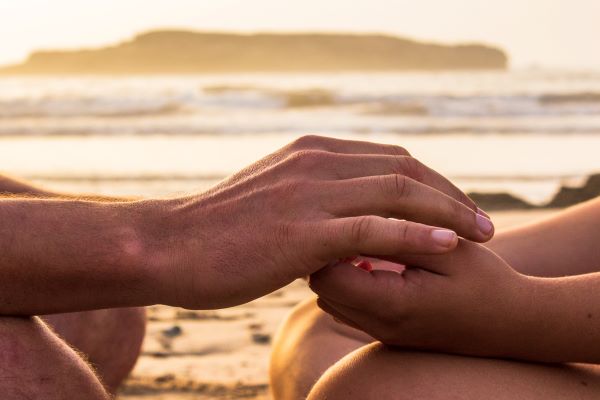 Two hands interlaced with sand and the ocean behind