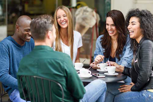 A group of five people sit around a table outside. They are smiling and laughing.