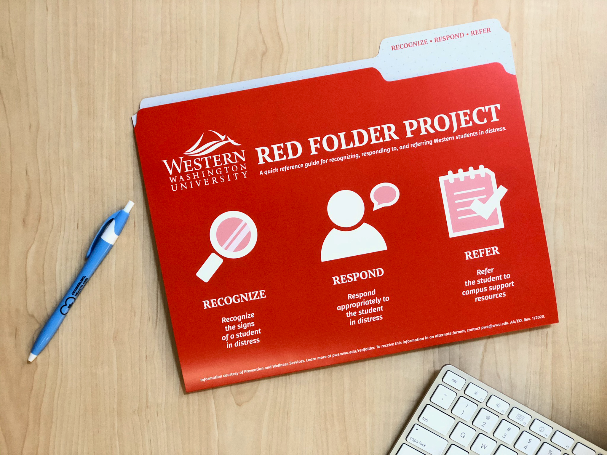 A red file folder, computer keyboard, and a blue pen on a desktop