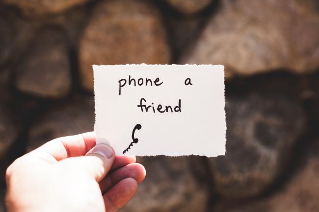 Hand holding a note image center with black text that reads "phone a friend" and rocks appear in the background