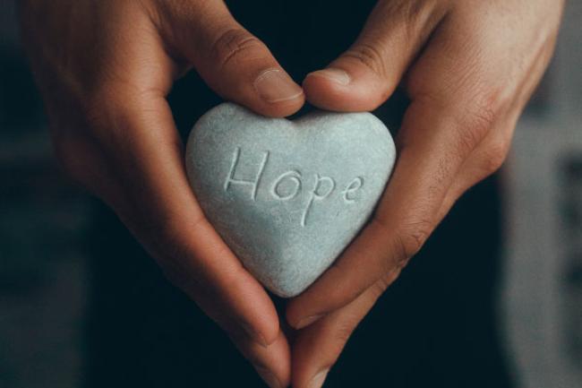 Hands holding a rock etched with the word "hope"