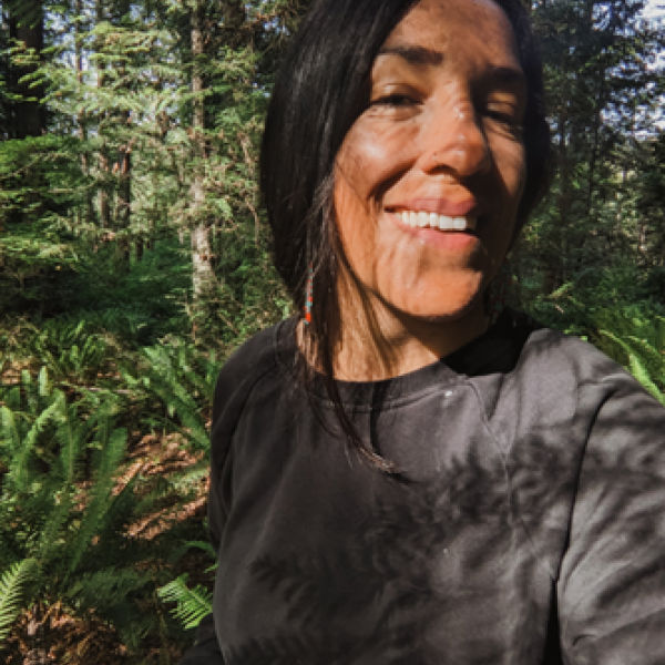Felicia, an Outdoor Wellness Mentor, smiles outdoors in the forest with shadows across her face